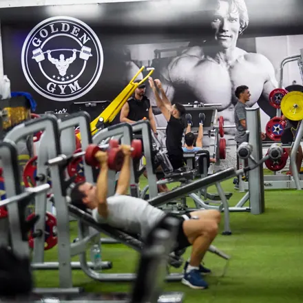 Socio entrenando pecho con mancuernas frente al escudo de Golden Gym